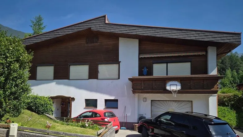Traditionelles Haus mit Holzfassade, weißem Putz und integrierter Garage, umgeben von Grün.