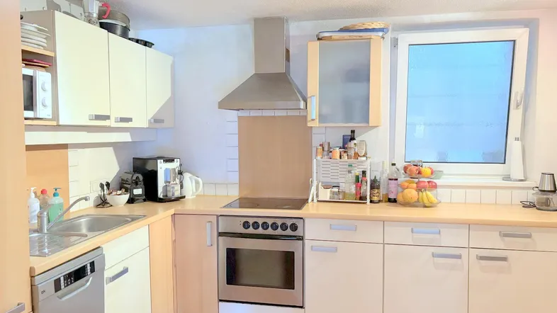 Funktionale Küche mit hellen Schränken, Terrakotta-Fliesenboden und Fenster für Tageslicht.