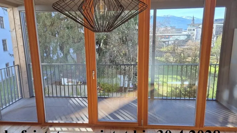 Heller Innenraum mit großen Glasfronten, die den Blick auf den Balkon und die grüne Umgebung freigeben.