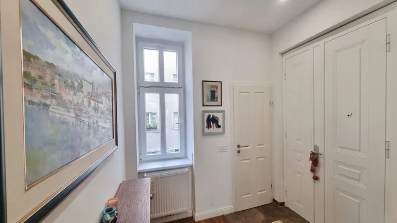 Helle Diele mit Holzboden, Fenster und Garderobenbereich, die zum Eingang führt.