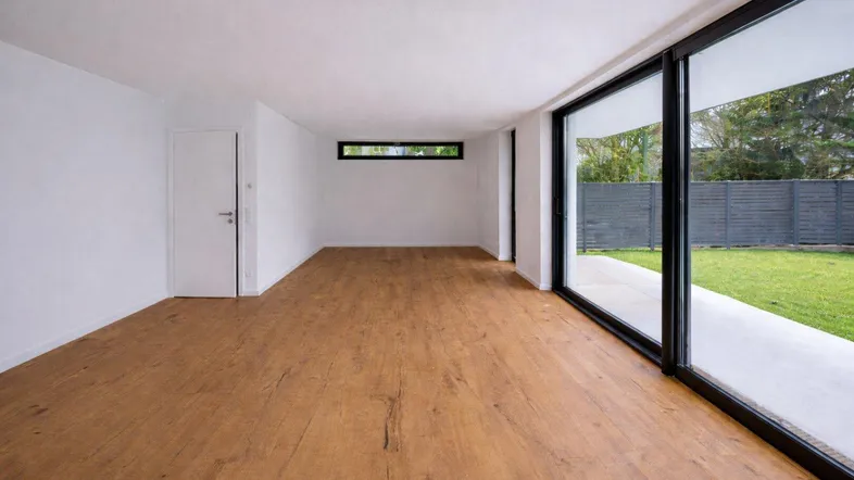 Helles, leeres Zimmer mit Holzboden und großen Schiebetüren zum Gartenbereich.