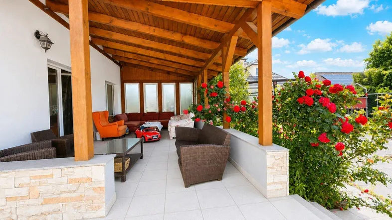 Überdachte Terrasse mit Holzbalken, Gartenmöbeln und blühenden Rosen.