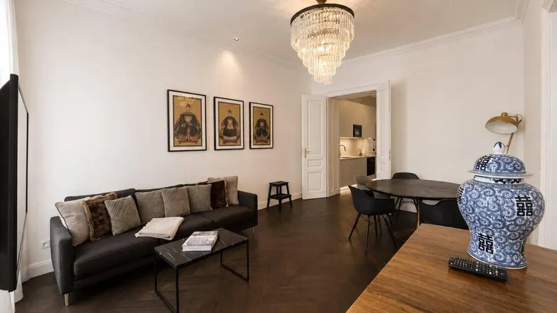 Helles Wohn- und Esszimmer mit dunklem Fischgrätparkett, modernem Kronleuchter und stilvoller Einrichtung.