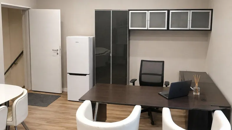 Modernes Büro mit Schreibtisch, Stühlen, Kühlschrank und Wandregalen, ideal für Arbeitszwecke.