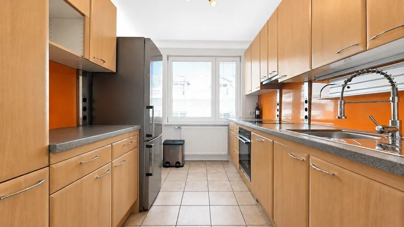 Helle Küche mit Holzschränken, orangefarbenem Fliesenspiegel, Fliesenboden und Fenster.