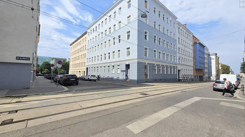 Gebäude an einer Straßenecke mit hellblauer Fassade und vielen Fenstern unter blauem Himmel.
