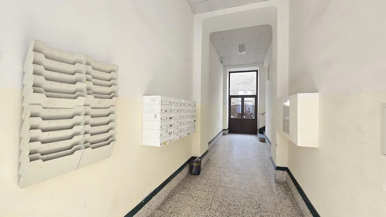 Langer, schmaler Flur mit Briefkästen an der Wand und einer Eingangstür am Ende.