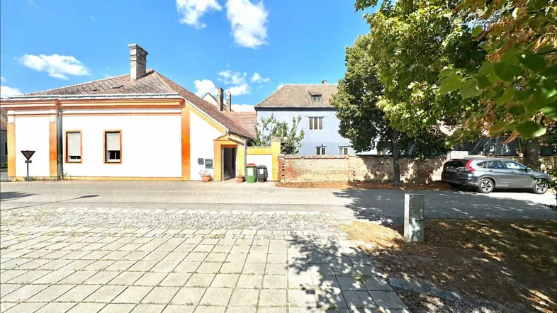 Ansicht der Gebäudefassade von der Straße aus mit gepflastertem Vorplatz und Bäumen.