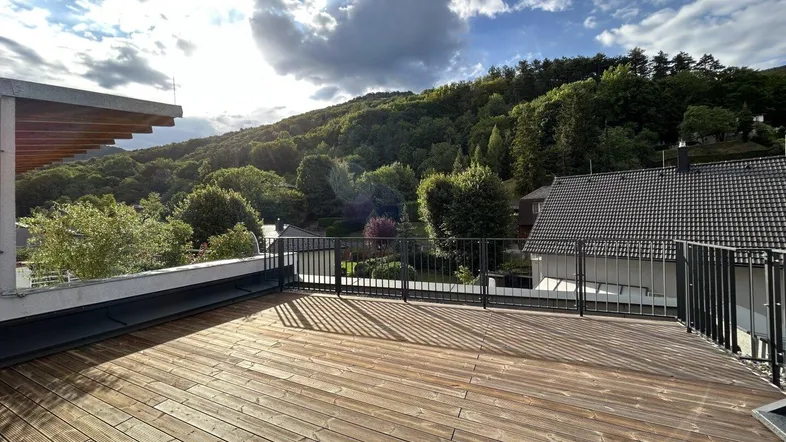 Große Holzterrasse mit weitem Blick auf die bewaldete Hügellandschaft unter sonnigem Himmel.