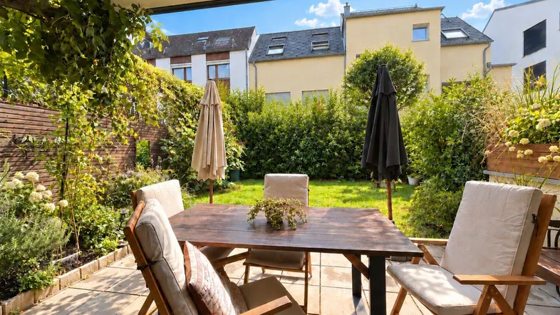 Geräumige Terrasse mit Gartenmöbeln, umgeben von üppigem Grün und Blick auf die Nachbarschaft.