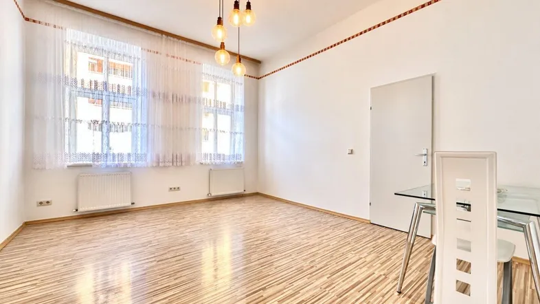 Helles Zimmer mit Parkettboden, großen Fenstern und moderner Deckenleuchte, ideal als Wohn- oder Essbereich.