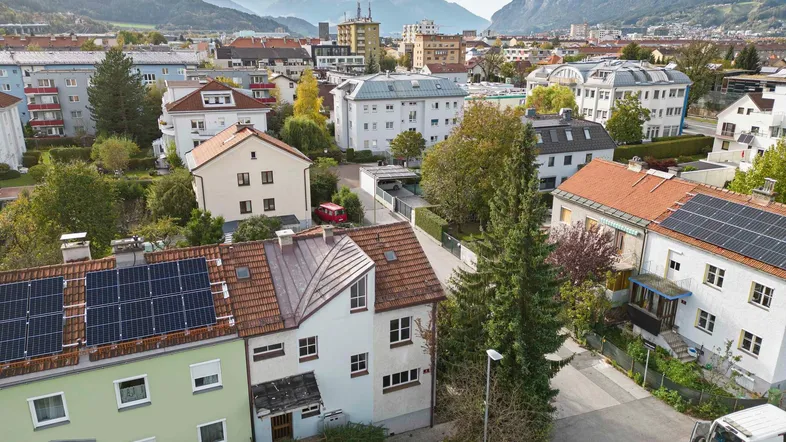 Luftaufnahme einer Wohnsiedlung mit Häusern, Gärten und Bergblick im Hintergrund.