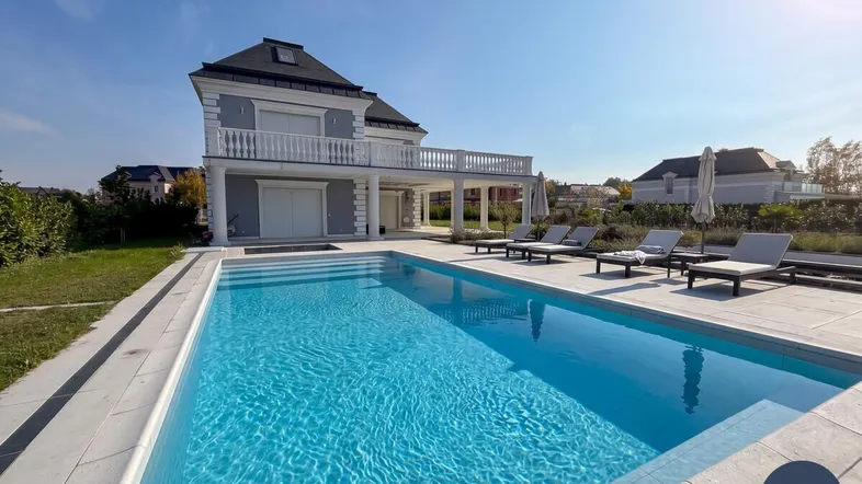 Elegante Villa mit großem Außenpool und Liegebereich unter blauem Himmel.