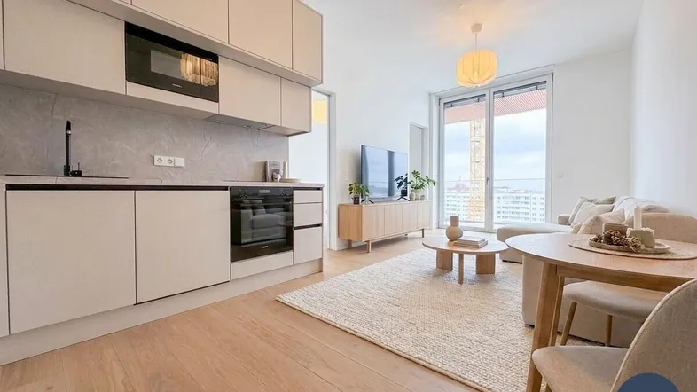 Heller offener Wohn-Essbereich mit integrierter Küche, Holzboden und Zugang zum Balkon.