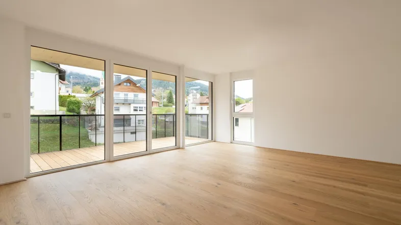 Heller Wohnraum mit Eichenparkettboden, großen Fenstern und Zugang zu einem Balkon mit Bergblick.