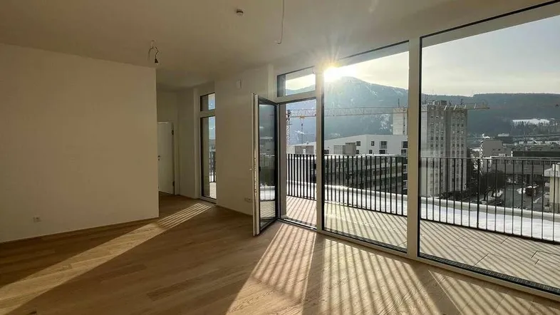 Helles Wohnzimmer mit Holzboden, großen Fenstern und Zugang zum Balkon, bietet einen weiten Blick.