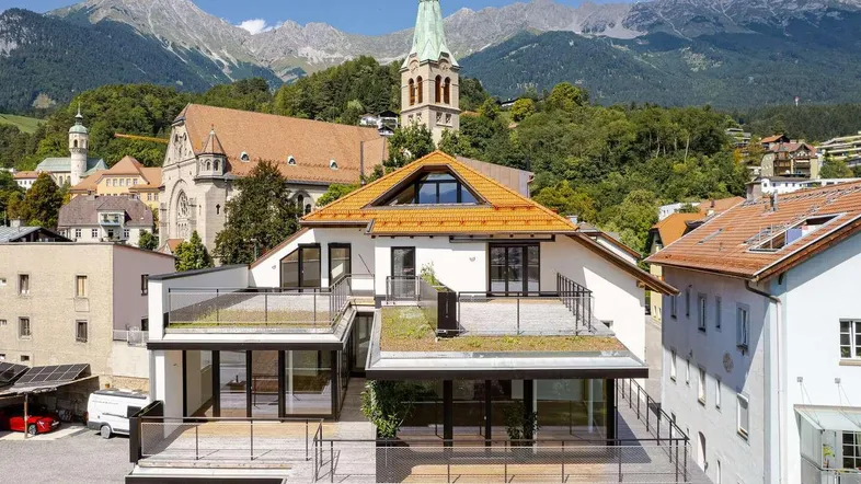 Moderne Architektur mit mehreren Terrassen und Gründach, umgeben von traditionellen Gebäuden und Bergen.