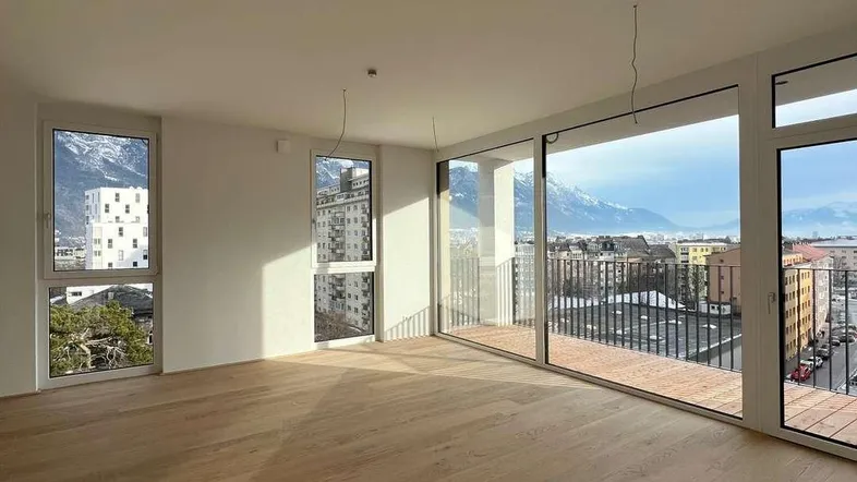 Heller, leerer Wohnraum mit großen Fenstern, Holzboden und Bergblick in einem Neubau.