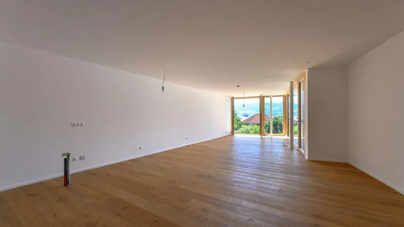 Geräumiges, helles Wohnzimmer mit Holzboden und großen Fenstern, die einen weiten Blick ins Grüne bieten.