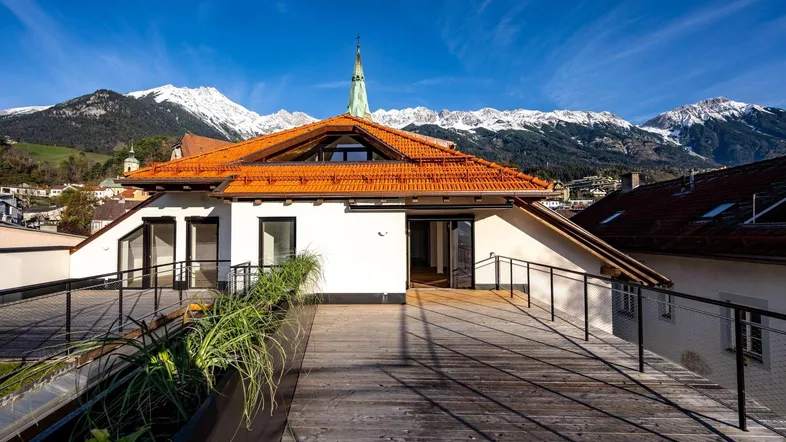 Große Dachterrasse mit Holzboden, Pflanzen und beeindruckendem Blick auf die schneebedeckten Berge.
