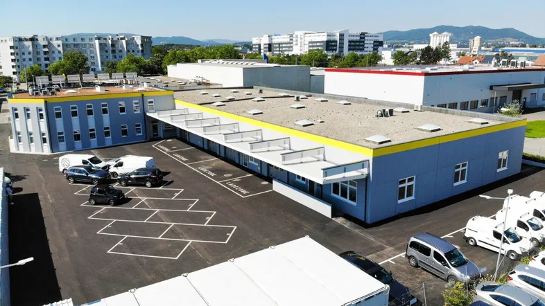 Luftaufnahme eines modernen Gewerbekomplexes mit mehreren Gebäuden und großzügigen Parkflächen unter blauem Himmel.