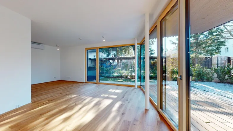 Helles Wohnzimmer mit Holzboden und großen Fenstern, die Zugang zur Terrasse und zum Garten bieten.