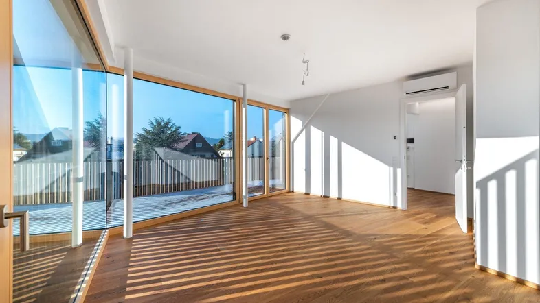 Helles Wohnzimmer mit großen Fenstern, Holzboden und Zugang zu einer Terrasse, durchflutet von Sonnenlicht.