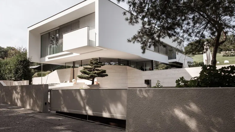 Moderne, weiße Villa mit klaren Linien und großen Glasflächen, umgeben von Grün.