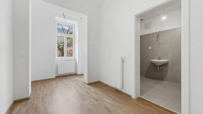 Heller, leerer Raum mit Parkettboden und Zugang zu einem Badezimmer.