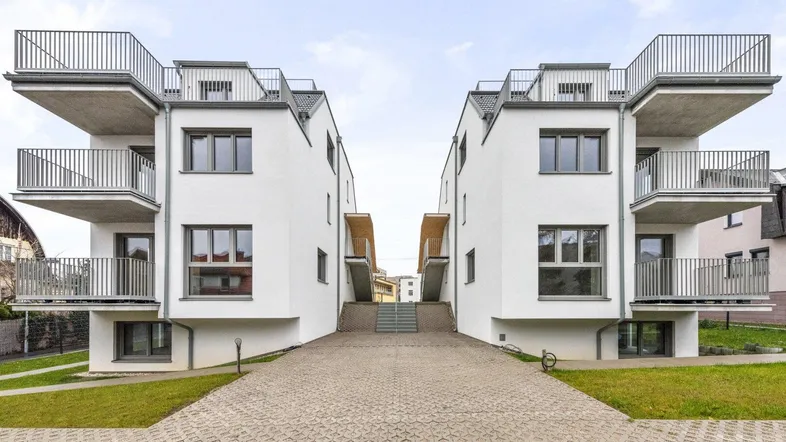 Moderne weiße Mehrfamilienhäuser mit Balkonen und gepflegter Außenanlage unter bewölktem Himmel.
