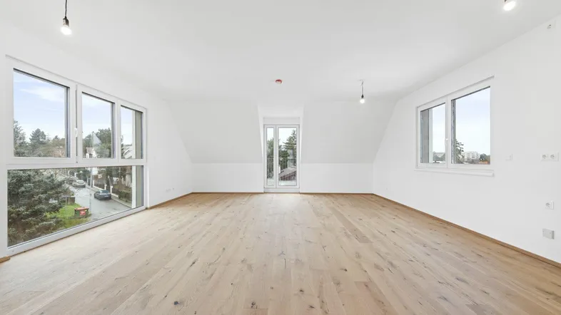 Geräumiger, heller Raum im Dachgeschoss mit Holzboden, großen Fenstern und Zugang zu einem Balkon.