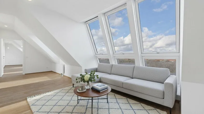 Helles Wohnzimmer in einer Dachgeschosswohnung mit großen Dachfenstern, modernem Sofa und Holzboden.