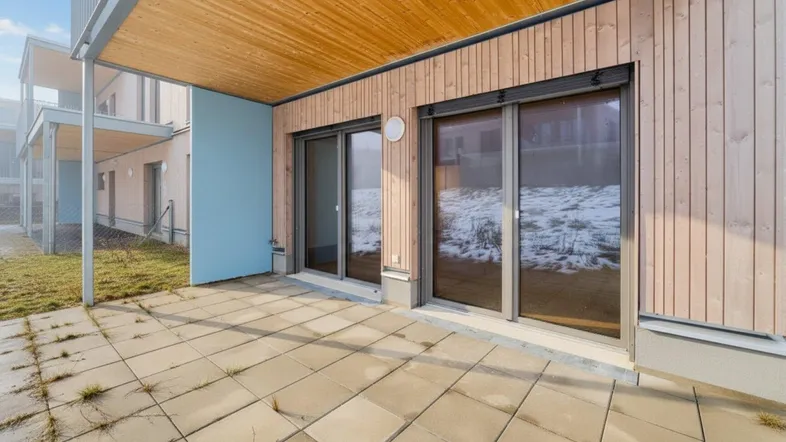 Gepflasterte Terrasse mit Holzwand und Überdachung, angrenzend an eine Grünfläche.