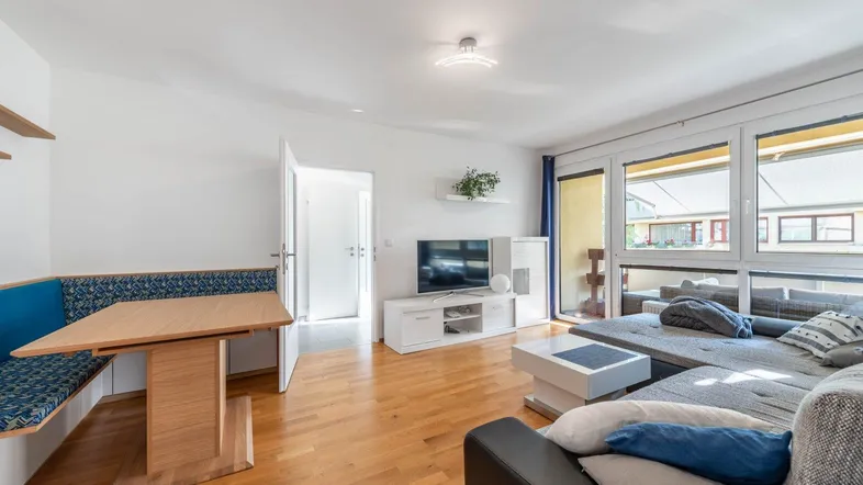 Helles Wohn- und Esszimmer mit Holzboden, großem Sofa und Zugang zum Balkon.
