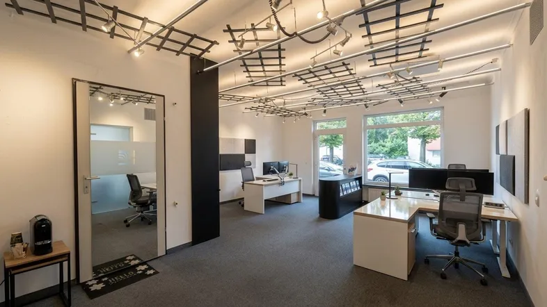 Modernes Büro mit mehreren Arbeitsplätzen, Teppichboden und auffälliger Deckenbeleuchtung.