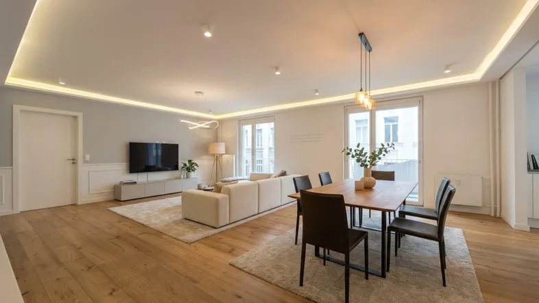 Helles Wohn- und Esszimmer mit Holzboden, moderner Einrichtung und Zugang zu einem Balkon.