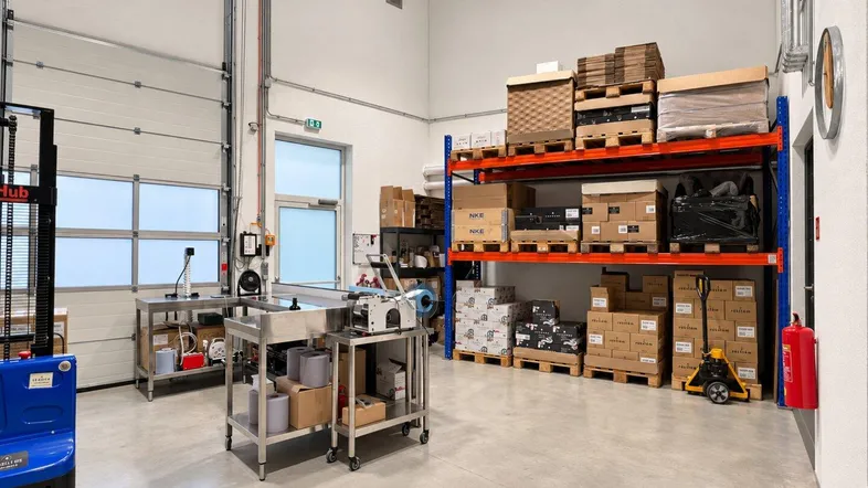 Geräumiger Lagerbereich mit hohen Decken, Regalen voller Kartons und industrieller Ausstattung, inklusive Gabelstapler.