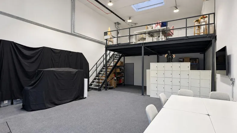 Geräumiger Büroraum mit hoher Decke, Teppichboden und einer Metallkonstruktion für eine Galerie.