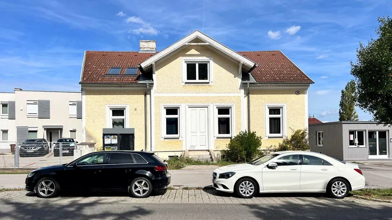 Traditionelles gelbes Haus mit Ziegeldach und zwei geparkten Autos auf der Straße davor.