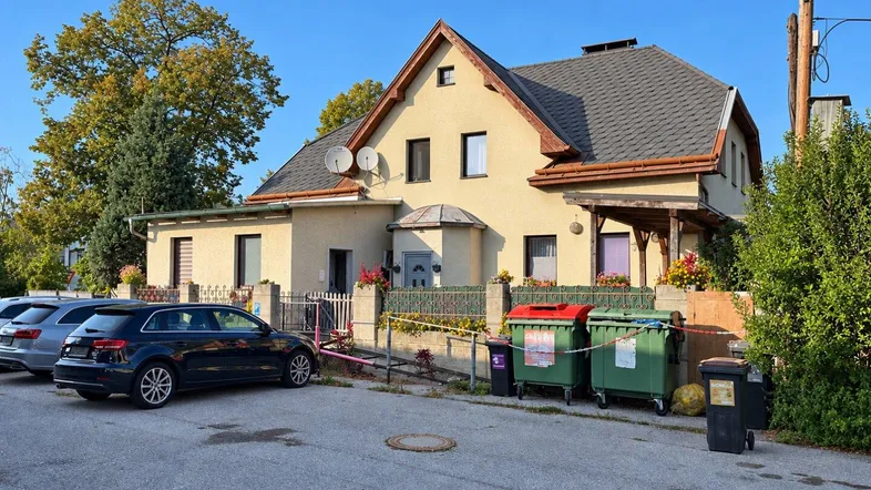 Vorderansicht des Hauses mit Satteldach, Vorgarten und parkenden Autos auf der Straße.