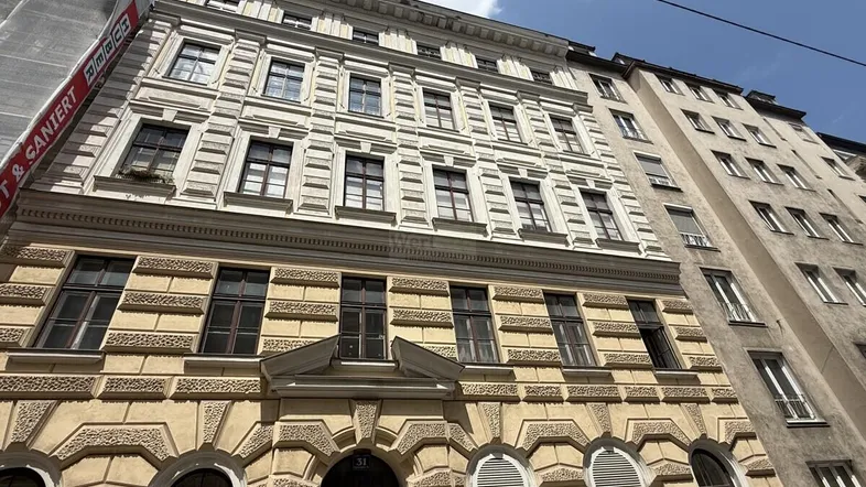 Historische Fassade eines Altbaus mit Gerüst an der Seite unter blauem Himmel.