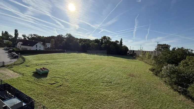 Weitläufige Grünfläche unter strahlendem Himmel, umgeben von Bäumen und Häusern.