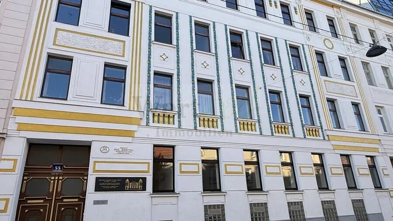 Historische Fassade eines Mehrfamilienhauses mit dekorativen Elementen und vielen Fenstern zur Straße.