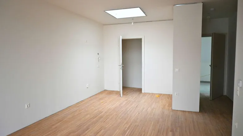 Helles, unmöbliertes Zimmer mit Holzparkettboden und einer Deckenleuchte, bereit zum Erstbezug.