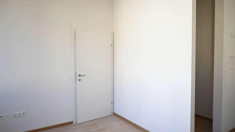 Heller Innenraum mit weißen Wänden, einer Tür und hellem Holzfußboden, bereit zur Einrichtung.