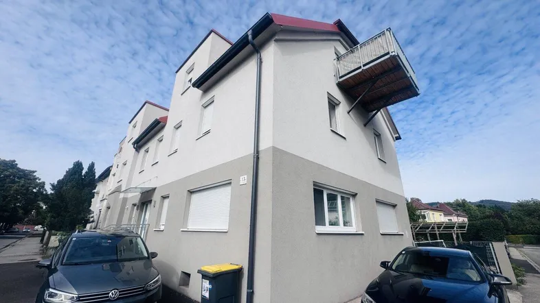 Mehrfamilienhaus mit moderner Fassade und kleinem Balkon unter bewölktem Himmel.