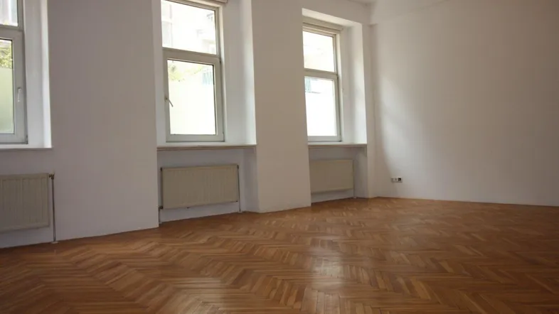 Helles Zimmer mit Fischgrätparkettboden und mehreren Fenstern, bereit zur individuellen Gestaltung.