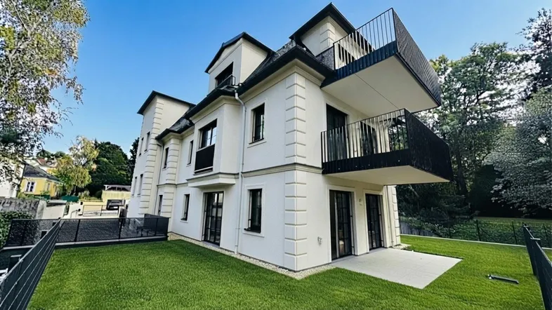 Modernes Mehrfamilienhaus mit weißer Fassade, schwarzen Balkonen und gepflegtem Rasen.