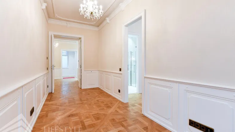 Eleganter Flur mit Fischgrätparkett, weißer Wandvertäfelung und Kronleuchter, der zu weiteren Räumen führt.
