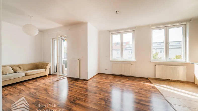 Helles Wohnzimmer mit Parkettboden und Zugang zu einem kleinen Balkon.